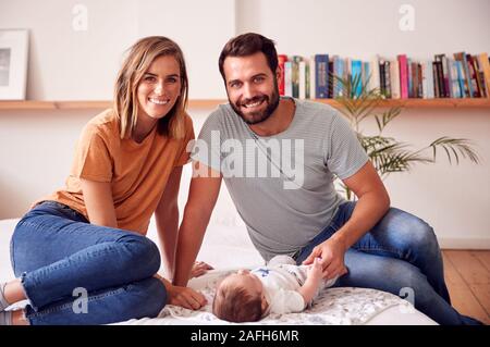 Portrait Of Loving Parents With Newborn Baby Lying On Bed At Home In Loft Apartment Stock Photo