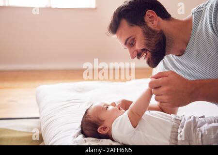 Loving Father Lying With Newborn Baby On Bed At Home In Loft Apartment Stock Photo