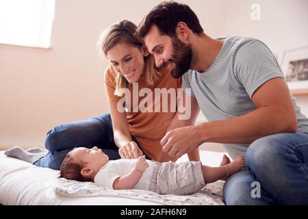 Loving Parents With Newborn Baby Lying On Bed At Home In Loft Apartment Stock Photo