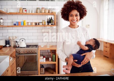 Portrait Of Smiling Mother Holding Sleeping Baby Son In Kitchen