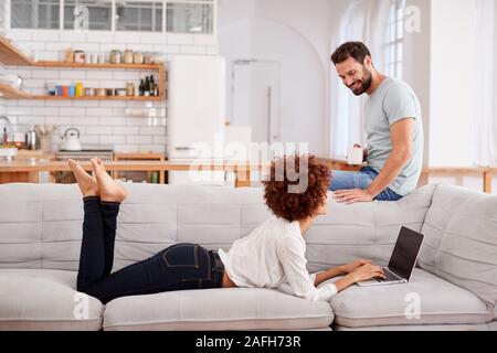 Couple Relaxing On Sofa At Home Looking At Laptop Together