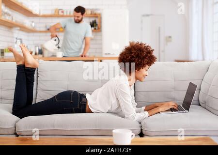 Woman Relaxing Lying On Sofa At Home Looking At Laptop Stock Photo