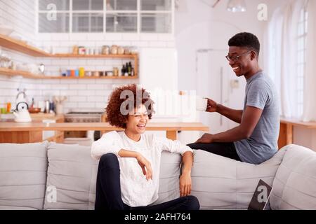 Young Couple Relaxing On Sofa At Home Together And Laughing Stock Photo