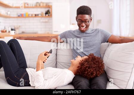 Young Couple Relaxing On Sofa At Home Looking At Mobile Phone Together Stock Photo