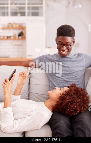 Young Couple Relaxing On Sofa At Home Looking At Mobile Phone Together Stock Photo