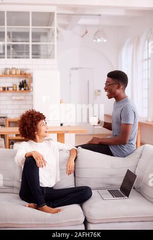 Young Couple Relaxing On Sofa At Home Together And Laughing Stock Photo