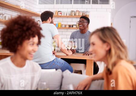 Two Couples Relaxing On Sofa At Home With Glass Of Wine Talking Together Stock Photo