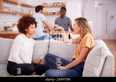 Two Couples Relaxing On Sofa At Home With Glass Of Wine Talking Together Stock Photo
