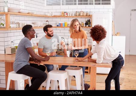 Two Couples Relaxing In Kitchen At Home With Glass Of Wine Talking Together Stock Photo