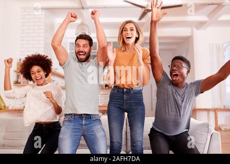 Excited Group Of Friends Sitting On Sofa Watching Sports On TV And Celebrating Stock Photo