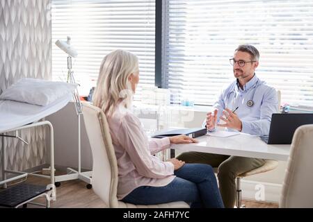 Mature Female Patient In Consultation With Doctor Sitting At Desk In Office Stock Photo