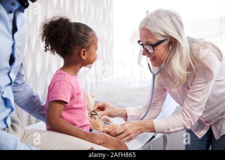 Female Doctor Giving Teddy Bear Medical Exam On Family Consultation In Office