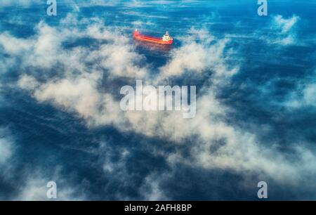 Aerial view of cargo container  ship sails in sea fog, crane vessel working for delivery of delivery containers. Stock Photo