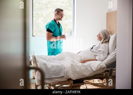 Surgeon Visiting And Talking With Mature Female Patient In Hospital Bed Stock Photo