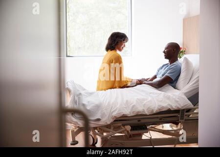 Wife Visiting And Talking With Patient Husband In Hospital Bed Stock Photo