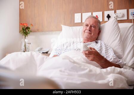 Male Senior Patient Lying In Hospital Bed Watching Television Stock Photo
