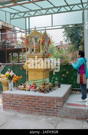 A devout Buddhist worshipper waves sticks of incense in front of several Buddha statues outside a temple in Elmhurst, Queens, New York City. Stock Photo