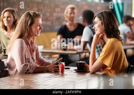 Two Female Friends Sitting At Table In Coffee Shop And Talking Stock Photo