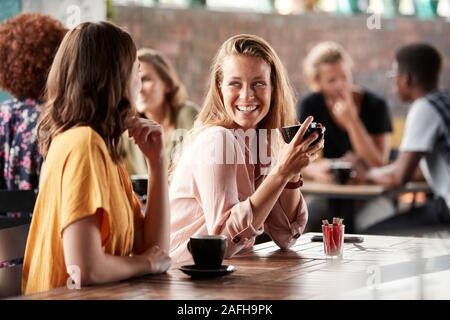 Two Female Friends Sitting At Table In Coffee Shop And Talking Stock Photo