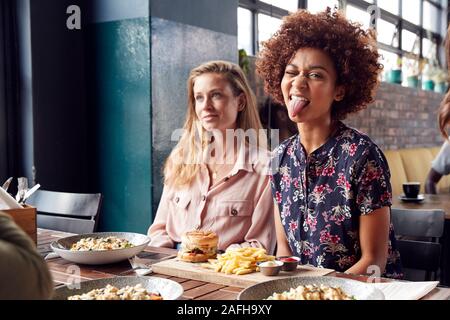 Woman Pulling Funny Face As She Meets With Friends For Drinks And Food In Restaurant Stock Photo