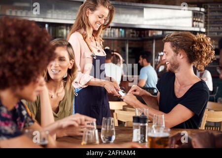 Waitress Holds Credit Card Machine As Customer Pays Bill In Bar Restaurant