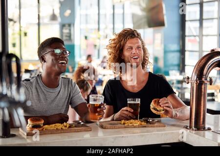 Two Male Friends Eating Food And Drinking Beer In Sports Bar Stock Photo