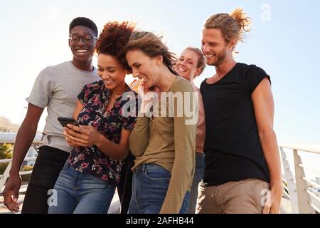 Smiling Young Friends Looking At Selfie On Outdoor Footbridge Together Stock Photo