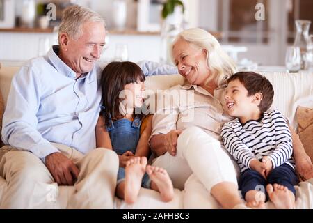 White senior couple and their grandchildren sitting on a sofa together smiling at each other Stock Photo