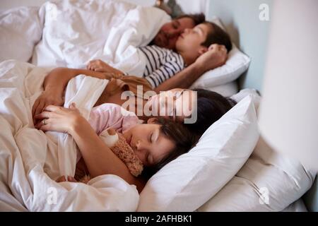 Mid adult parents sleeping in bed with their two young children, waist up, close up