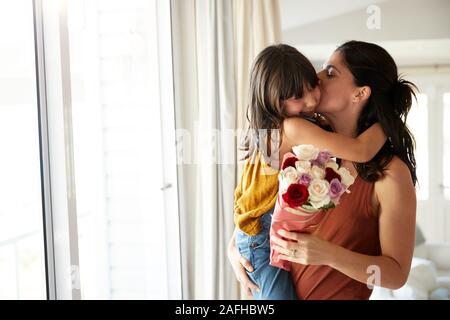 Mid adult woman holding her daughter, who’s given her a bunch of flowers on her birthday, waist up