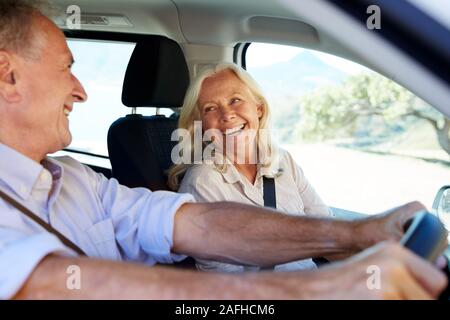 Senior white couple driving in their car, looking at each other, side view, close up