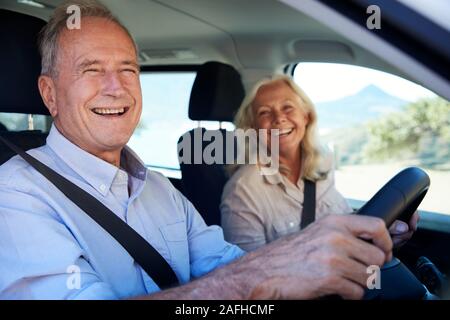 Happy senior white couple driving in their car, smiling to camera, side view, close up