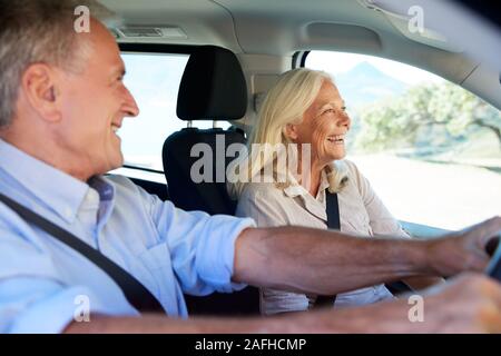 Happy senior white couple driving in their car, smiling, side view, close up