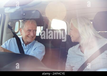 Senior white couple driving in their car smiling to each other, seen through front windscreen Stock Photo