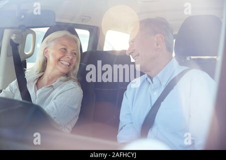 Happy senior white couple driving in their car smiling at each other, seen through front windscreen