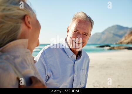 Senior white couple walking on a beach, looking at each other and smiling, waist up, close up Stock Photo
