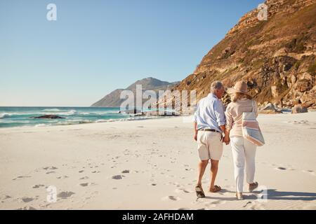 Senior white couple walking on a beach together holding hands, full length, back view Stock Photo