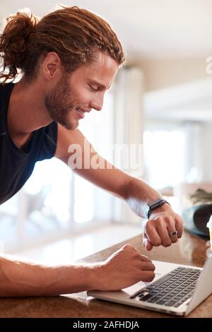 Millennial white man checking fitness app on smartwatch using laptop after a workout, side view Stock Photo