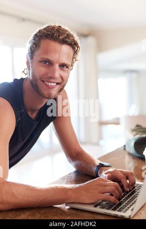 Millennial white man checking fitness app on laptop after a workout smiling to camera, vertical Stock Photo