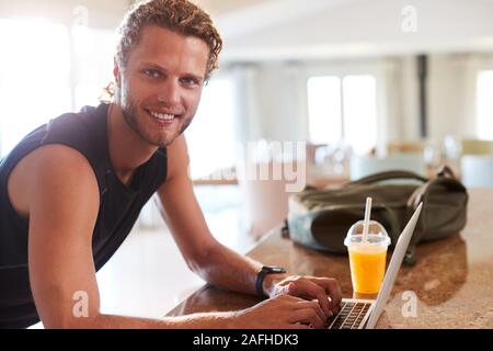 Millennial white man checking fitness app on laptop at home after a workout, smiling to camera Stock Photo