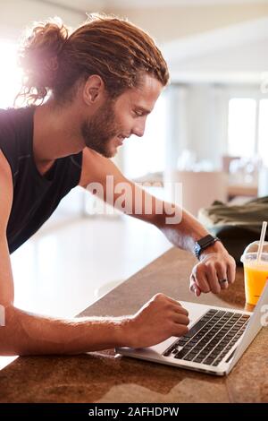 Millennial white man checking fitness app on watch and laptop after a workout, side view, vertical Stock Photo