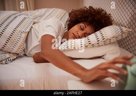 Millennial African American woman half asleep in bed, reaching out for the alarm clock, close up