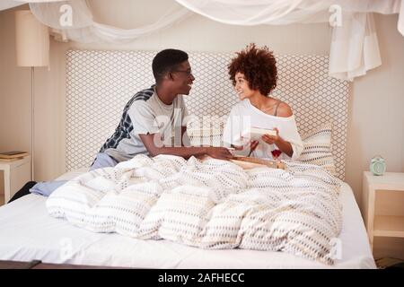 Millennial African American man giving his partner breakfast and gifts in bed to celebrate Stock Photo