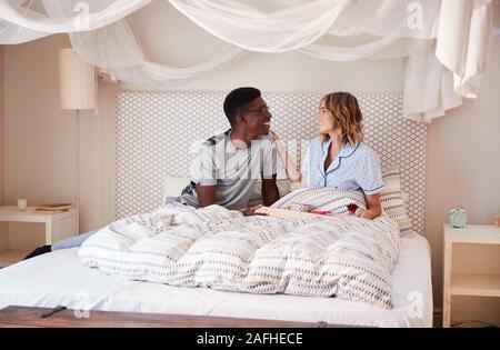 Millennial African American man serving his white female partner breakfast in bed, looking at each other Stock Photo