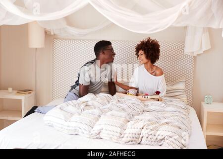 Millennial African American man giving his partner breakfast and gifts in bed to celebrate Stock Photo