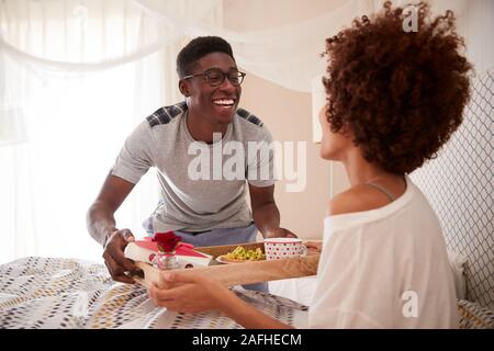 Millennial African American couple celebrating, man bringing his partner breakfast in bed, close up