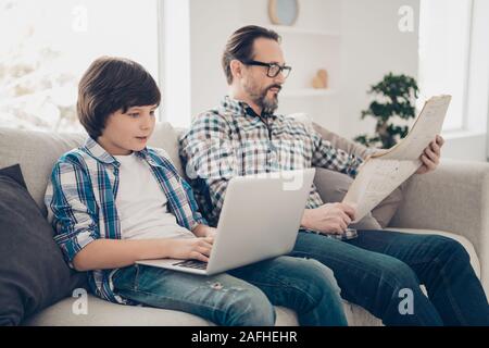 Profile side view portrait of two nice attractive focused concentrated serious guys dad and pre-teen son sitting on sofa typing on laptop reading news Stock Photo