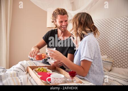 Millennial white couple celebrating with champagne,  breakfast and gifts in bed, close up Stock Photo
