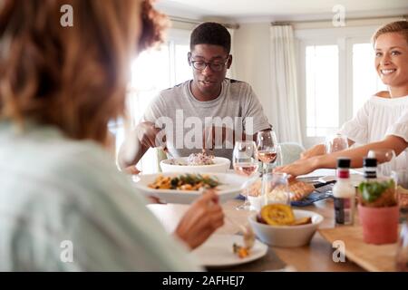 Millennial friends eating lunch together at a sitting at dinner table, close up Stock Photo