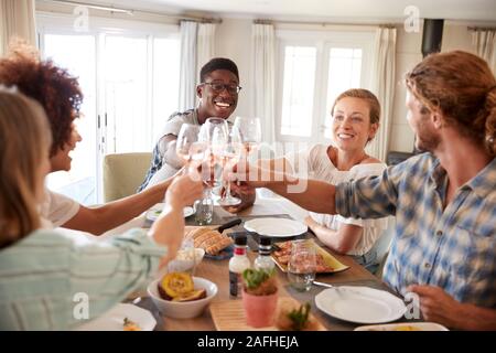 Millennial friends sitting at a dining table making a toast during lunch, close up Stock Photo